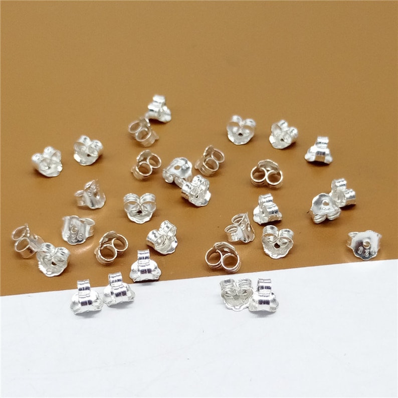 May include: A collection of silver earring backs, also known as earring stoppers, for securing earrings. The backs are made of metal and have a butterfly design.