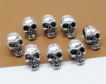 Puede incluir: Ocho cuentas de calavera plateadas con detalles elaborados. Las cuentas son pequeñas y tienen un aspecto ligeramente envejecido.
