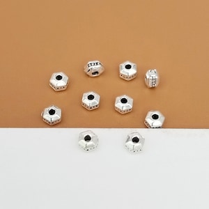 May include: Ten silver-toned metal beads with a hexagonal shape and a small hole in the center. The beads have a decorative design around the edges.