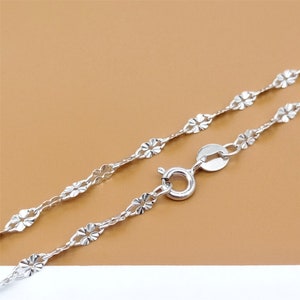 May include: A silver chain necklace with a delicate flower design. The chain is made of small, linked flower shapes.