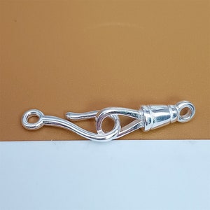 May include: Silver-toned clasp with a hook and loop design. The clasp is made of metal and has a polished finish.