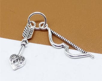 May include: Silver charm featuring a heart-shaped arrow with a bow and arrow design. The charm is made of metal and has a detailed design.