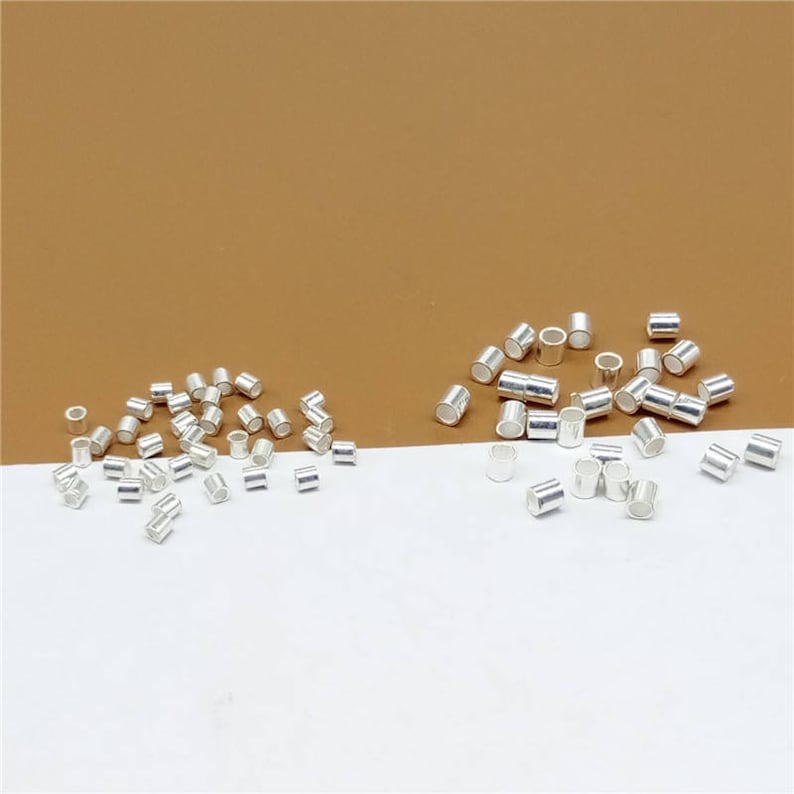 May include: A pile of silver jump rings, a type of jewelry finding, on a white surface. The jump rings are small and round, with a diameter of about 5mm. They are used to connect different pieces of jewelry together.