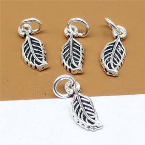 Op de afbeelding: Vier zilveren bladeren bedels met een zwarte geoxideerde afwerking. Elke bedel heeft een kleine lus om te bevestigen aan een ketting, armband of andere sieraden.