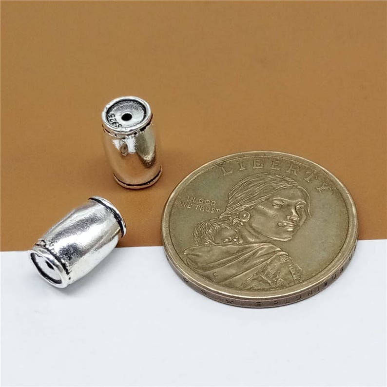 K&ouml;nnte beinhalten: Zwei silberne, tonnenf&ouml;rmige Perlen aus Metall. Die Perlen sind glatt und haben eine gl&auml;nzende Oberfl&auml;che. Die Perlen sind etwa 2,5 cm lang.