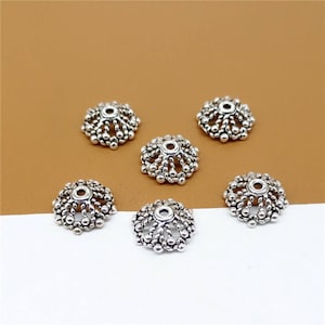 May include: Six silver-toned metal bead caps with a decorative, scalloped design. The caps have a small hole in the center for threading.