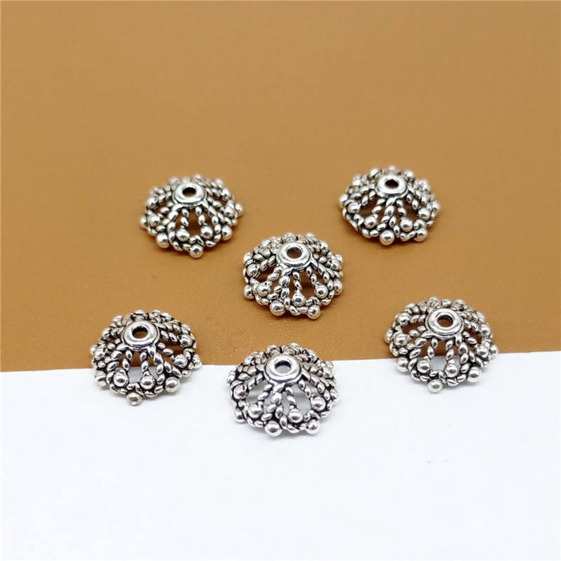 May include: Six silver-toned metal bead caps with a decorative, scalloped design. The caps have a small hole in the center for threading.