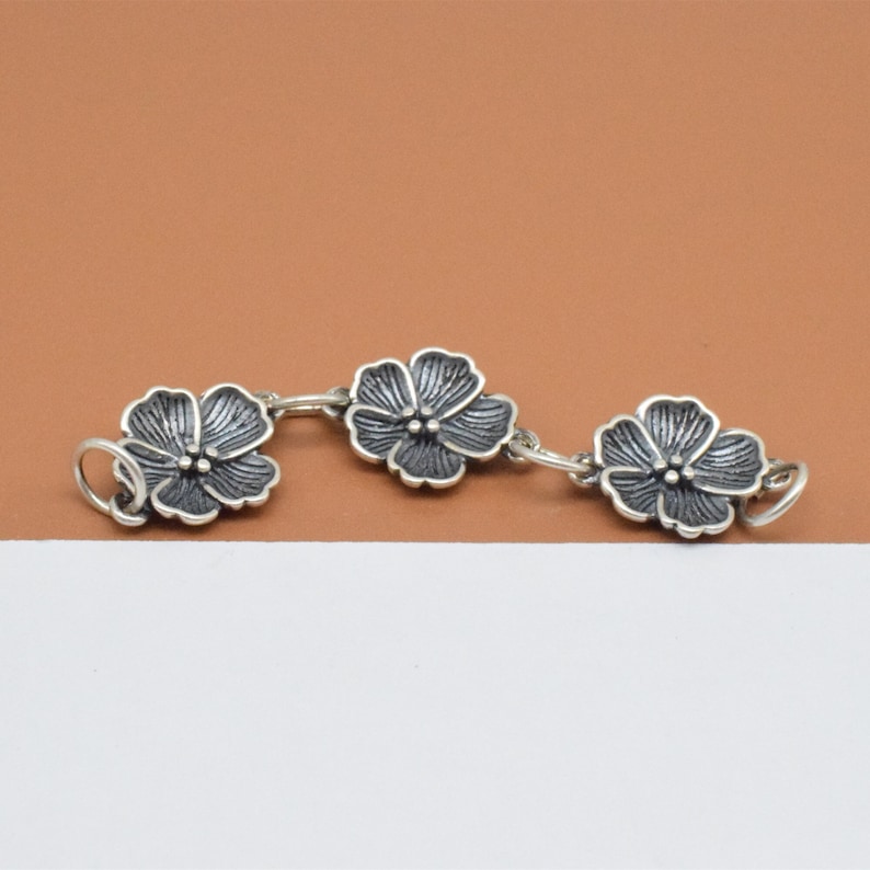 May include: A silver chain bracelet with three flower charms. The flowers are silver with a dark gray finish.