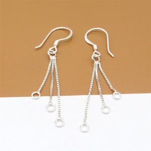May include: A pair of silver dangle earrings with three chains and four small circles at the end of each chain.