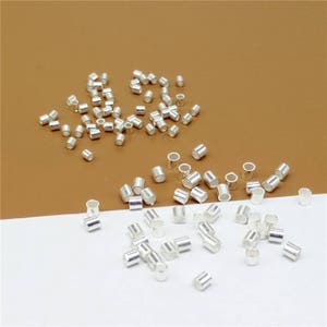 May include: A large quantity of silver-toned metal jump rings. The jump rings are small and round, and they are scattered on a brown surface.