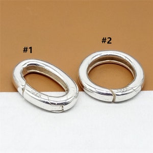 Op de afbeelding: Twee zilveren ovale springringen met een sluiting. De ringen zijn aan de zijkant gemarkeerd met "925". De ring aan de linkerkant is gemarkeerd met "#1" en de ring aan de rechterkant met "#2".