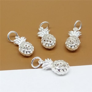 Puede incluir: Cuatro abalorios de piña de plata con un bucle en la parte superior para sujetarlos a joyas. Los abalorios están detallados con un diseño de piña y tienen un acabado brillante.