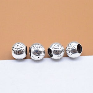 Könnte beinhalten: Vier silberne Charm-Perlen mit geometrischem Design. Jede Perle hat eine erhabene Diamantform in der Mitte mit Linien, die vom Diamanten ausstrahlen.