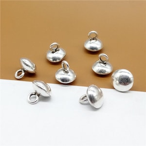May include: Silver tone metal button charms with a loop on top. The charms are round and have a slightly domed shape.
