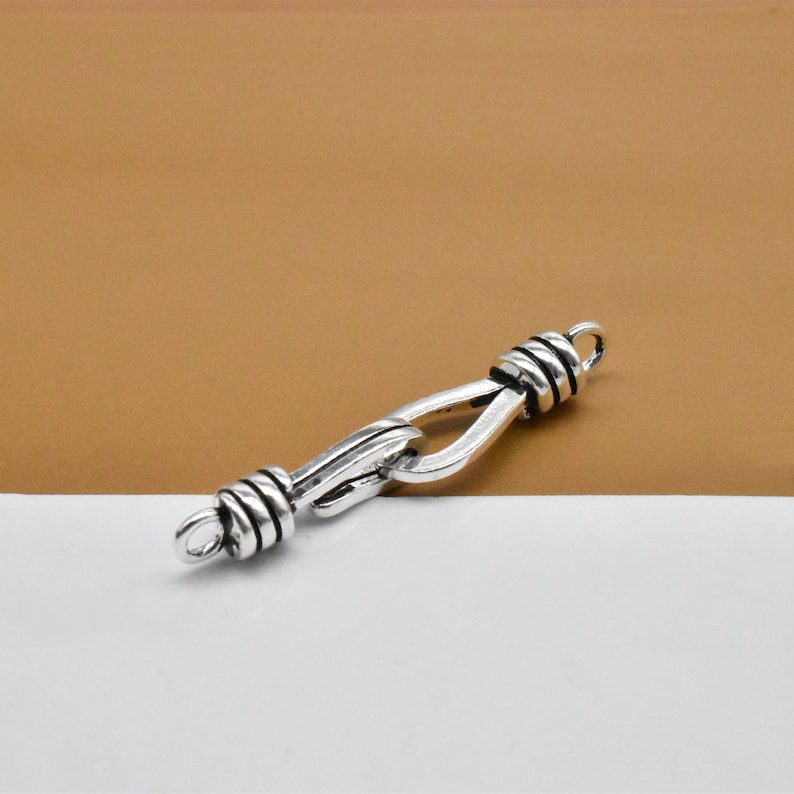 May include: Silver-toned metal clasp with a twisted design. The clasp is open and ready to be attached to a chain or bracelet.