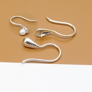 May include: Two silver earring hooks with a small pearl on one of the hooks. The hook is marked with "S925" indicating it is made of sterling silver.