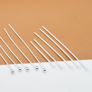 May include: A set of silver head pins with round and flat heads. The pins are arranged in a row on a white surface.