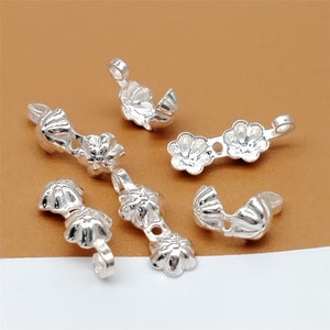 May include: Six silver-toned metal jewellery findings with a floral design. The findings have a loop on one end and a decorative flower on the other end.