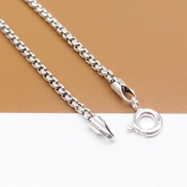 May include: A silver chain necklace with a lobster clasp closure. The chain is made of small, linked circles.