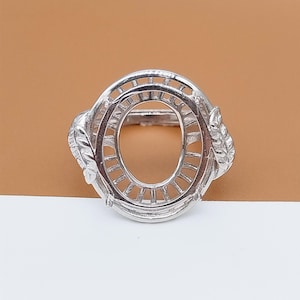 Può includere: Un castone per anello color argento con un centro ovale. L'anello presenta un design a foglie decorative su ciascun lato dell'ovale. Il castone ha un design traforato dettagliato attorno all'ovale.