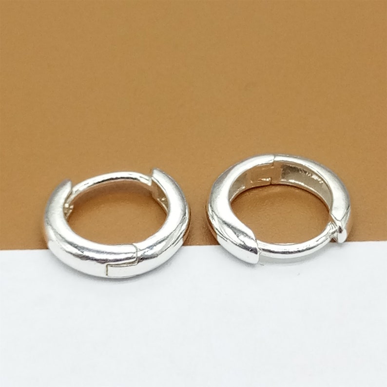 May include: A pair of silver hoop earrings. The earrings are small and have a simple design.