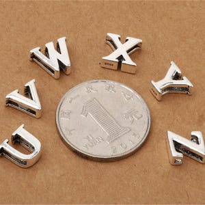 May include: Silver charm letters in the alphabet, including the letters U, V, W, X, Y, and Z. The charms are small and delicate, perfect for adding a personalized touch to jewelry.