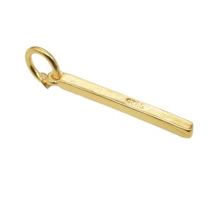 Peut inclure: Un charme en forme de barre en or avec une boucle en haut et l'inscription "G265" sur le côté.