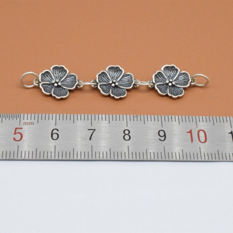 May include: Silver chain with three flower charms, measuring approximately 3 cm in length.