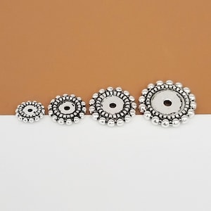 May include: Three silver metal round bead caps with a decorative design. The bead caps are different sizes.