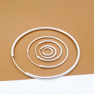 May include: Five silver hoop earrings of different sizes, arranged in a concentric circle pattern on a brown background.