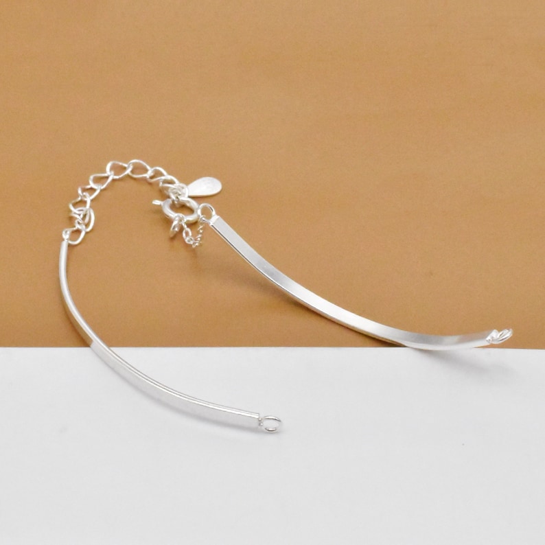 May include: A silver bracelet with a curved design and a lobster clasp closure.