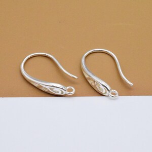 May include: Two silver earring hooks with a decorative design. The hooks are made of metal and have a smooth finish.