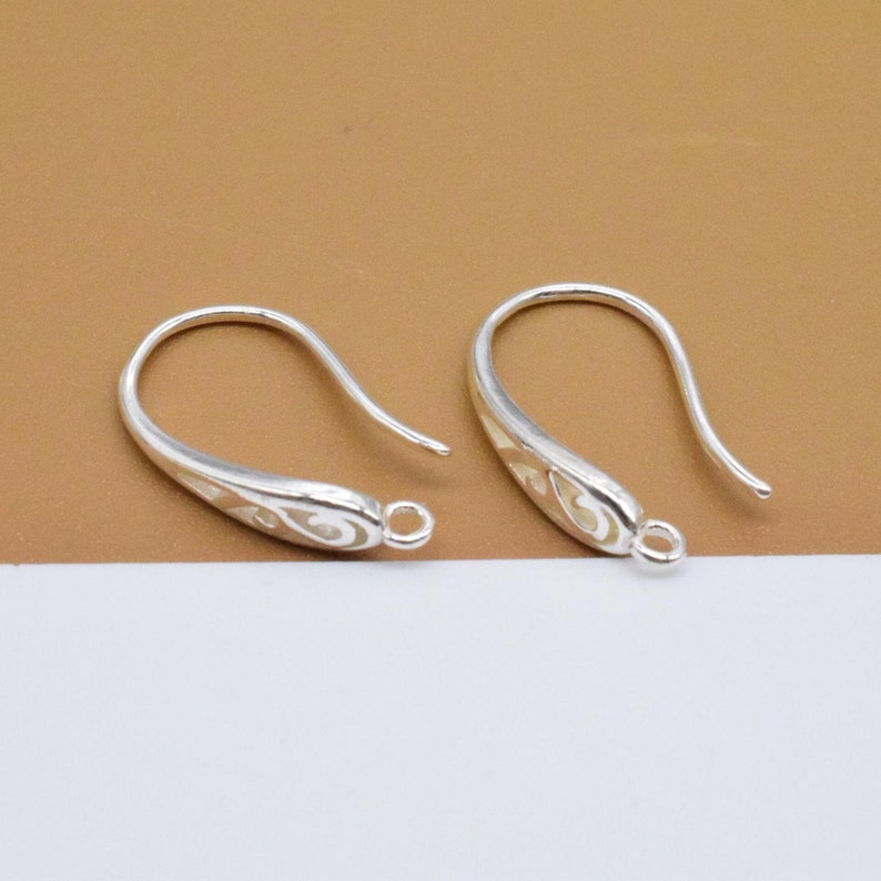 May include: Two silver earring hooks with a decorative design. The hooks are made of metal and have a smooth finish.