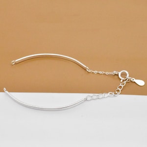 May include: A silver bracelet with a delicate chain and a curved bar design.