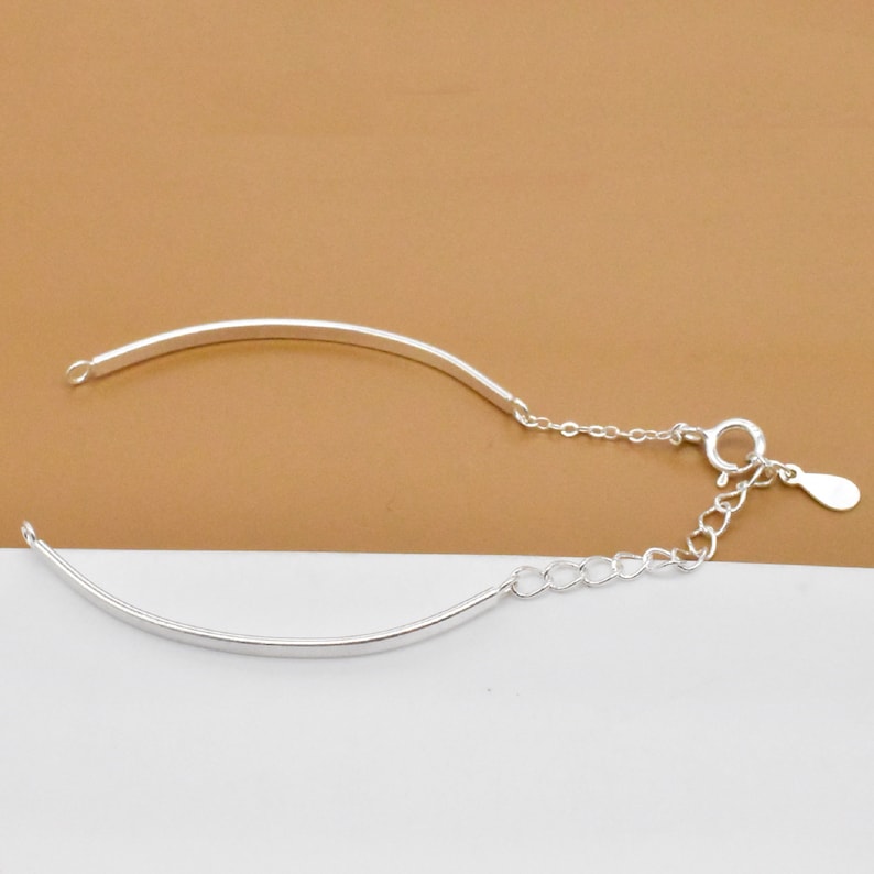 May include: A silver bracelet with a delicate chain and a curved bar design.