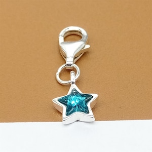 Puede incluir: Encanto de plata con un cristal azul verdoso en forma de estrella. El encanto tiene un cierre de langosta para sujetarlo a una pulsera o collar.