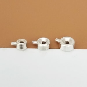 May include: Three silver metal knobs with a round shape and a small handle on the side. The knobs are different sizes.
