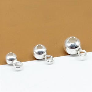 May include: Three silver bead caps with loops. The bead caps are different sizes. The smallest bead cap is on the left, the middle bead cap is in the center, and the largest bead cap is on the right.