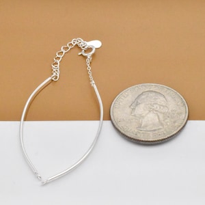 May include: A silver bracelet with a delicate chain and a clasp. The bracelet is shown next to a US quarter for size comparison.