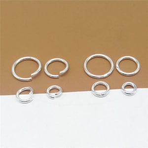 May include: A set of silver jump rings in various sizes. The jump rings are arranged in two rows, with the larger rings in the top row and the smaller rings in the bottom row.