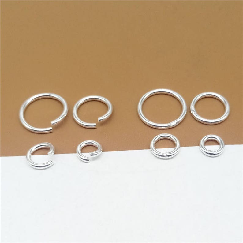 May include: A set of silver jump rings in various sizes. The jump rings are arranged in two rows, with the larger rings in the top row and the smaller rings in the bottom row.