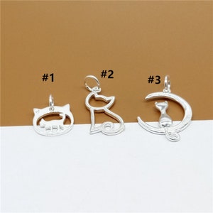 May include: Three silver cat charm pendants. The first charm is a circle with a cat silhouette inside. The second charm is a cat silhouette. The third charm is a crescent moon with a cat silhouette sitting on it.