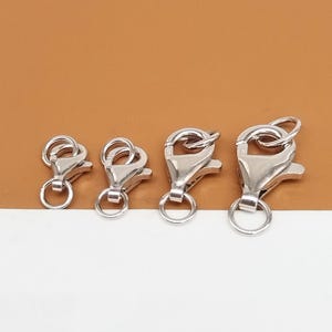 Könnte beinhalten: Vier silberne Hummer-Klauenschließen in verschiedenen Größen. Die Verschlüsse sind alle aus Metall und haben eine glänzende Oberfläche.