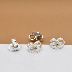 May include: Four silver earring backs with a scalloped design. The backs are designed to be used with post earrings.