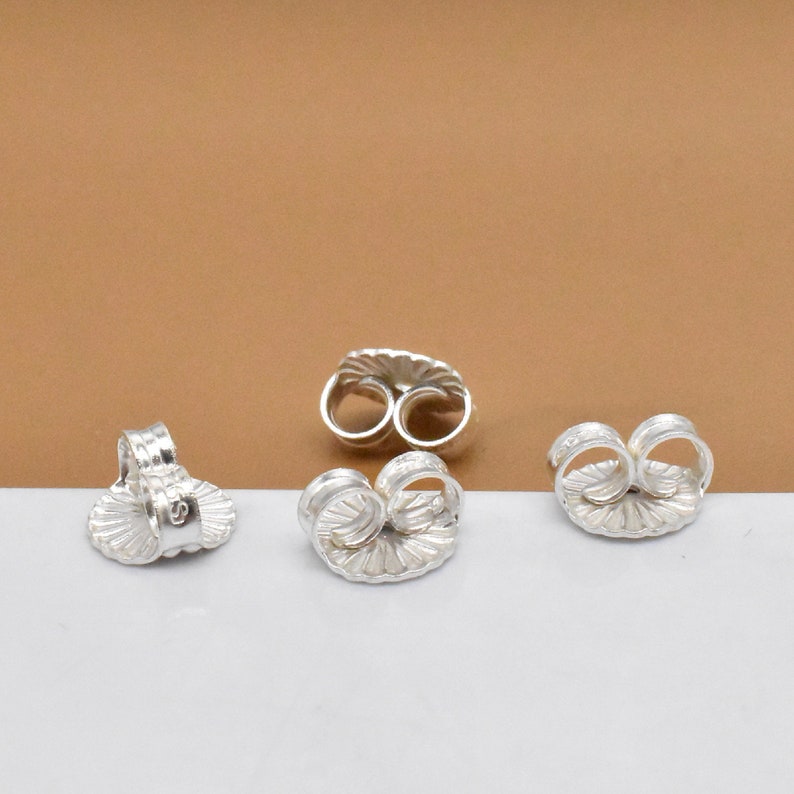 May include: Four silver earring backs with a scalloped design. The backs are designed to be used with post earrings.