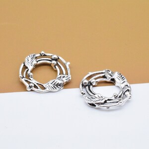 May include: Two silver-toned metal rings with a decorative design of leaves and berries. The rings are open and could be used for jewelry making or other crafts.