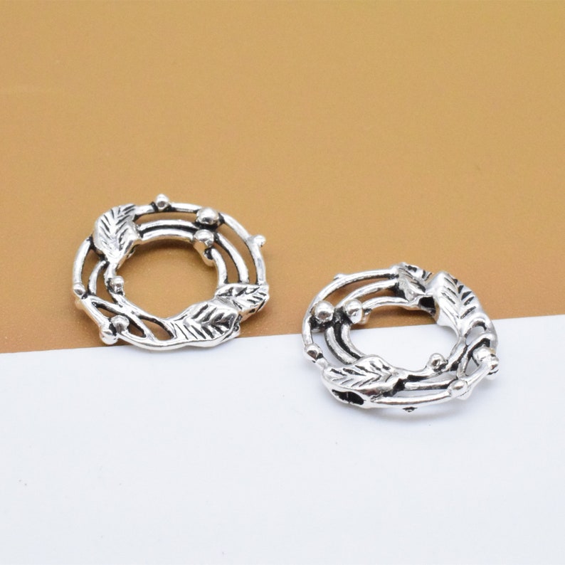 May include: Two silver-toned metal rings with a decorative design of leaves and berries. The rings are open and could be used for jewelry making or other crafts.