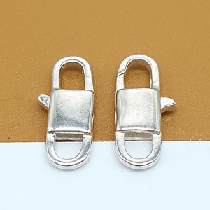 Puede incluir: Dos cierres de langosta plateados con un diseño rectangular. Los cierres están abiertos y listos para ser unidos a una cadena u otras joyas.