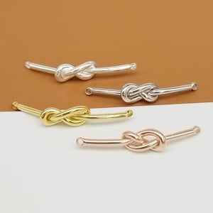 May include: Three silver, gold, and rose gold knot-shaped jewellery connectors. Each connector has a straight bar with a small hole at each end.