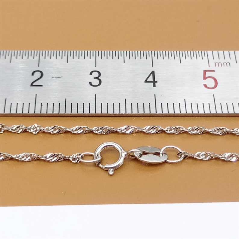 May include: A silver chain necklace with a lobster clasp. The chain is approximately 2 mm wide and is measured against a ruler.